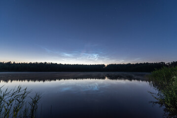 Noctilucent clouds over the forest lake in Latvia on June night