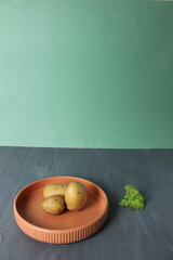 Raw potatoes on a plate on a gray green background. The concept of simple food. Art photography as art