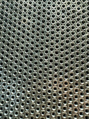 Intricate metal surface with circular and rectangular holes in closeup view, metal nuts