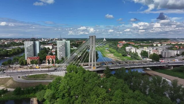 Flying away from pylons of the Emperor Otto Bridge in Magdeburg in a panoramic view. Sunny weather, cloudy sky. Apartment blocks, Elbe and skyline in the background, cars driving on the bridge.