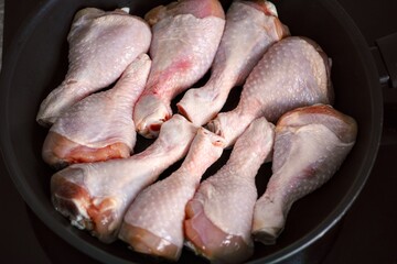 Raw chicken drumsticks in a frying pan ready to be cooked