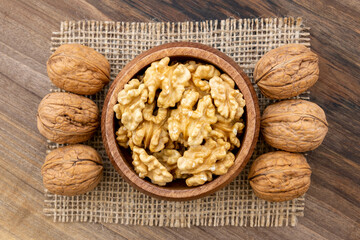 Overhead view of a bowl full of walnut kernels on a wooden surface. A piece of burlap and a few shelled walnut lying around