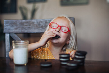 Little blond girl with red glasses with a glass of molk and oreo cookies