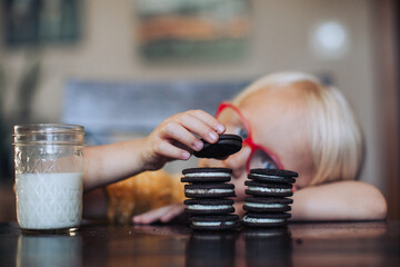 Little blond girl with red glasses with a glass of molk and oreo cookies