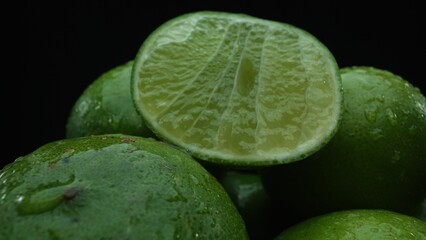 Slices of lime are meticulously arranged in a pile, set against a black background. Each lime slice is captured in stunning detail, its vibrant green hue and enticing texture. Close up. Comestible.