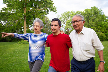 A family of three is walking through a park. The young man is wearing a red shirt and the adult woman is wearing a blue striped T-shirt. The woman points to something in the distance