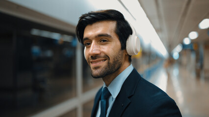 Closeup of smart business man wearing headphone and listening music while standing at train...
