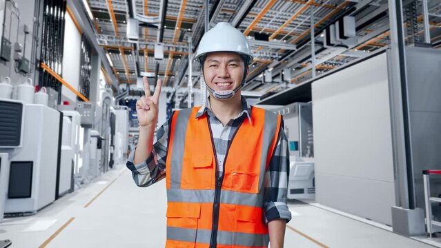 Asian Male Engineer With Safety Helmet Smiling And Showing Peace Gesture While Standing At Factory Digitalization