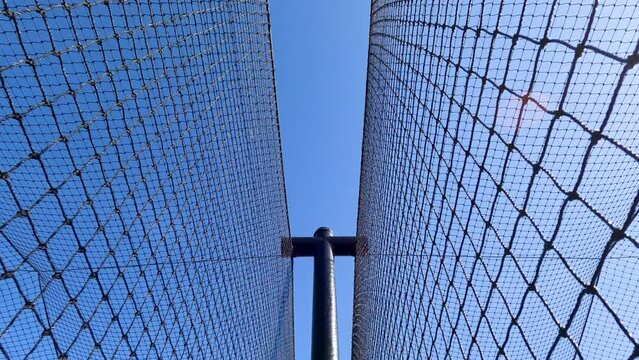Sports Nets Against a Clear Blue Sky. Looking up a sports netting used to enclose a batting cage. Stationary view with wind creating minimal motion in the netting. Metal post at the center of view.