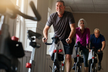 Spin class, senior or man on bike in workout or training for cycling progress, health or wellness. Gym, group challenge or confident elderly person on bicycle machine for fitness, exercise and cardio