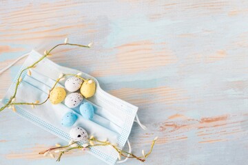 Color quail eggs in face medical and willow tree branch mask on wooden background. Coronavirus...