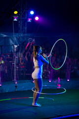 Young slim attractive circus gymnast woman performing live show with hula hoops on red arena with...