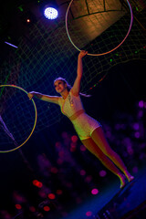 Obraz premium Young slim attractive circus gymnast woman performing live show with hula hoops on red arena with blue backlight, audience is excited