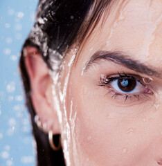Woman, half face and shower for cleaning in studio, washing and grooming for skincare on blue background. Female person, water and liquid for cosmetics or treatment and hydration, beauty and skin