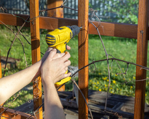 A man uses a cordless drill to assemble a wooden pergola, demonstrating home improvement and...
