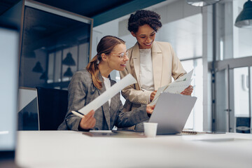 Two smiling business woman work together with documents to get the job done at the office