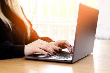 Young white caucasian woman working on computer on wooden table in home office. close up female businesswoman hands typing text on keyboard, surfing internet on modern laptop. mock up, top front view