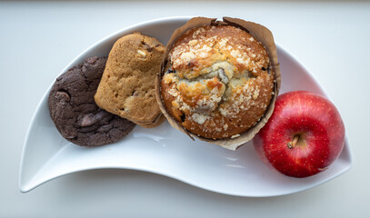Selection of goodies and a healthy red apple on a curved plate on white background.