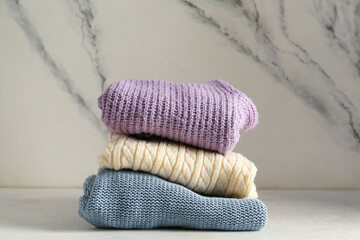 Stack of different stylish sweaters on light background