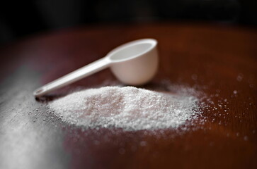 xylitol, sugar substitute, on a wooden surface with a plastic spoon (doser).
