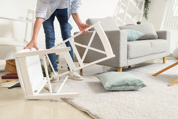 Woman taking broken chair from floor after earthquake at home