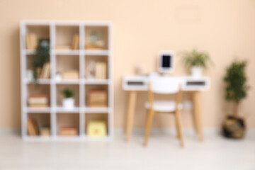 Interior of modern living room with workplace and bookshelf near beige wall, blurred view