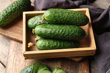 Box and boards with fresh green cucumbers on wooden background, closeup