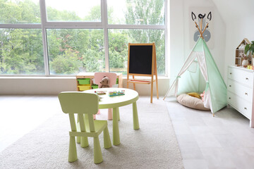Interior of light playroom with toys, teepee and chalkboard in kindergarten