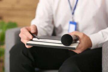 Male reporter with microphone and notebook sitting in armchair at studio, closeup
