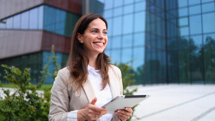Fototapeta premium Beautiful, young businesswoman enjoying outside, in front of her company building and using a digital tablet