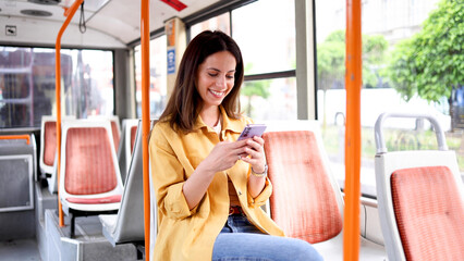 Beautiful, young woman riding in a city bus and using her smartphone