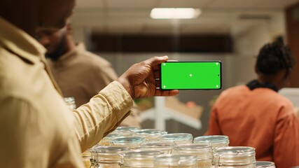 African american seller shows greenscreen display on mobile phone in local neighborhood market,...