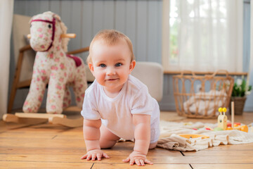 A baby is crawling on the floor in front of a rocking horse.