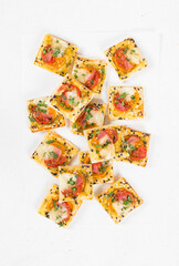 Mini appetizer square pies with tomatoes, ham, mozzarella, pesto, sesame seeds.  White background. Top view