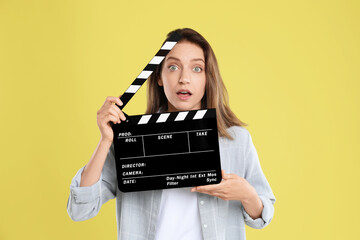 Making movie. Beautiful surprised woman with clapperboard on yellow background