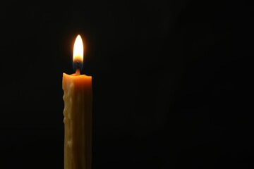 One burning church candle on black background, space for text