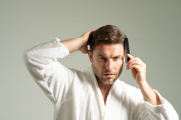 A man is brushing his hair with a comb while wearing a white robe. Concept of relaxation and self-care, as the man takes the time to groom himself. The white robe adds to the overall calm