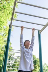 Obraz premium Young Man Doing Pull Ups on Outdoor Gym Equipment During Summer Day