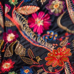 Macro photography of the detailed embroidery on a traditional garment, focusing on the vivid threads and complex patterns that define the textile's beauty