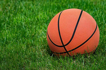 A basketball rests on green grass, seemingly ready for play. The ball is detailed with recognizable...