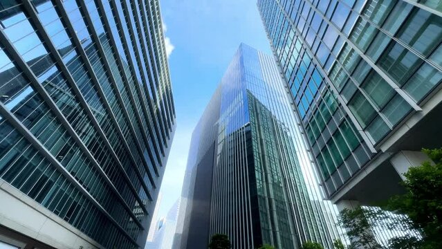 Modern skyscrapers reach towards a clear blue sky with green trees in the foreground