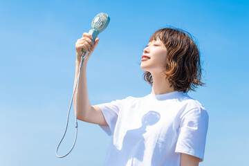 ハンディファンで涼む白いTシャツ姿の女性・熱中症対策