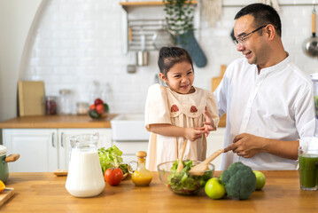 Joyful moment of father and daughter cooking together in modern kitchen, father guiding daughter prepares fresh salad with various vegetables and ingredients, healthy eating and home cooking at home