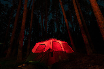Red, illuminated tent at night in the forest
