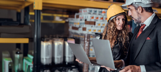 Engineer woman and businessman wearing a hardhat standing cargo at goods warehouse and check for control loading from Cargo freight ship for import and export by report on laptop. Teamwork concept