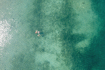 People swim in Greece transparent turquoise blue sea water with sandy bottom, aerial drone view.