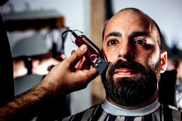 Barber cutting beard of customer with hair trimmer.