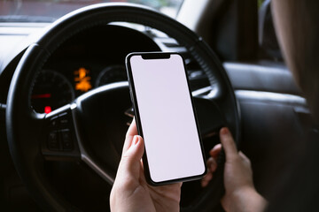 Woman sitting in a car and holding a smartphone with blank screen.
