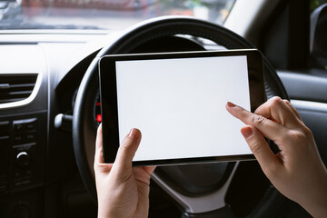 Woman sitting in a car and holding a tablet with blank screen.