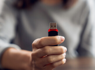 Hand holding usb flash drive with connecting to laptop at wooden table